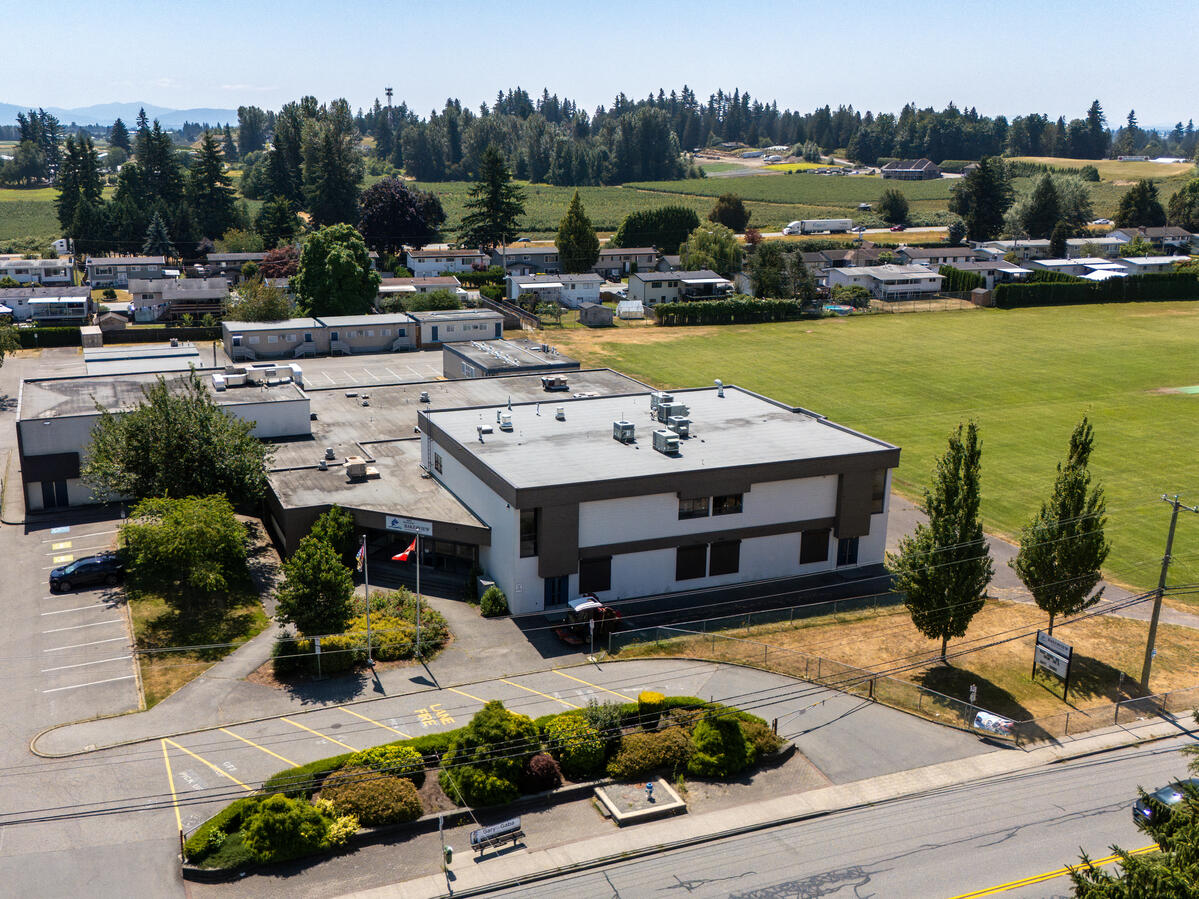 Exterior image of a secondary level school. It shows the front entrance and school field in the background. Along with a nearby neighbourhood and tree landscape in the distance.