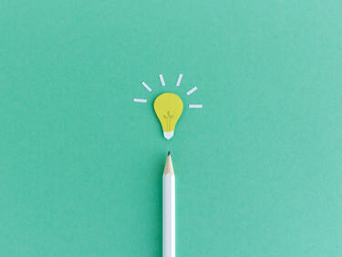 Creative composition of pencil with small paper light bulb glowing above on green background