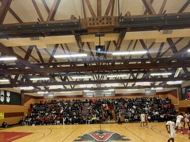 School gym filled with students and staff for a basketball game.