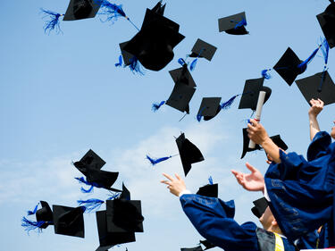 Blue sky with students throwing graduation caps into the air