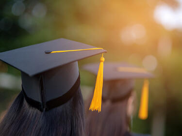 photo with two students wearing grad cap and gown. Black with yellow tassel