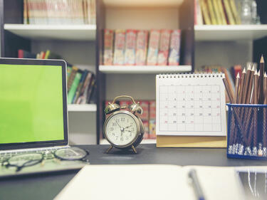 office desk with laptop, pencils and clock