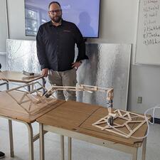 Two female students working their constructed design in Engineering class, male teacher stands and watches